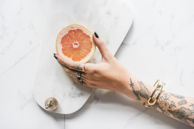 Mujer tatuada sosteniendo una naranja sobre un fondo de mármol