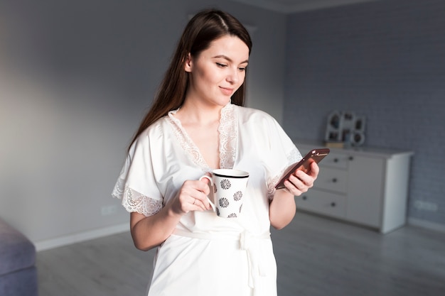 Mujer con taza usando teléfono inteligente