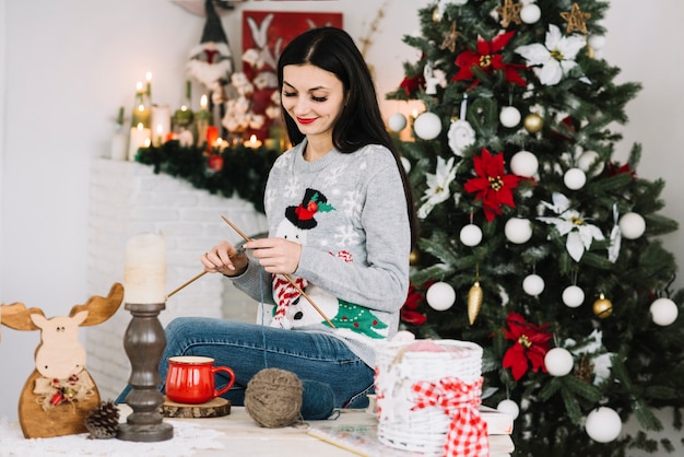 Mujer tejer cerca de arbol de navidad