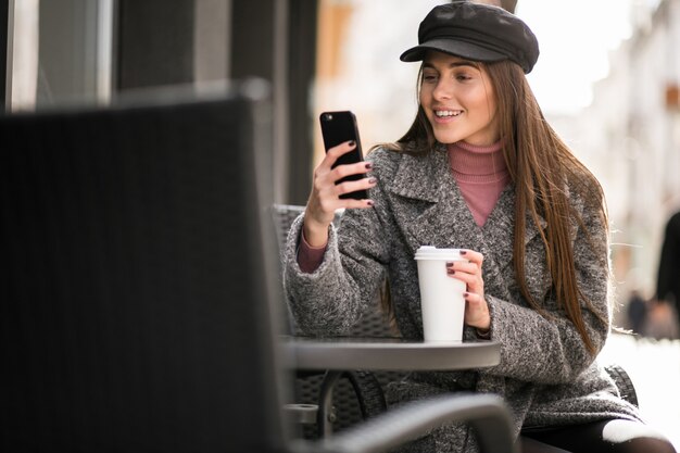 Mujer con teléfono y café sentado afuera del café