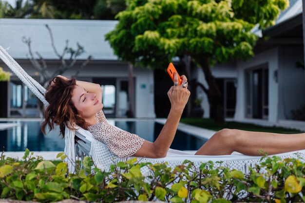 Mujer con teléfono descansando acostado en una hamaca con teléfono móvil