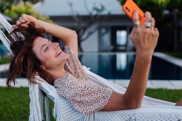 Mujer con teléfono descansando acostado en una hamaca con teléfono móvil