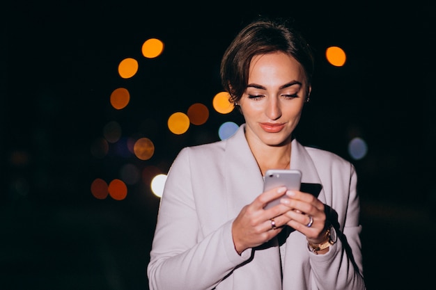 Mujer con teléfono fuera en la calle de noche