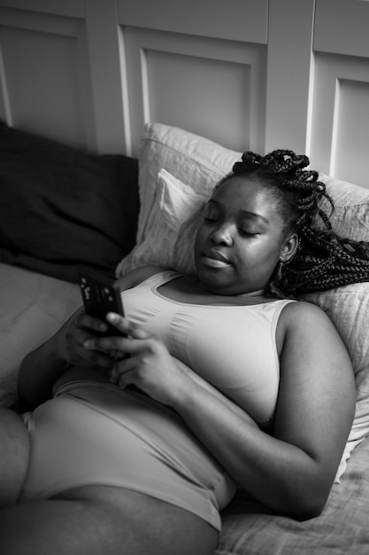 Mujer con teléfono inteligente en la cama tiro medio