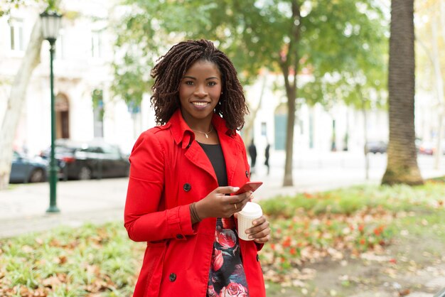 Mujer con teléfono inteligente y vaso de papel sonriendo