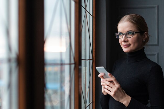 Mujer con teléfono mirando por la ventana