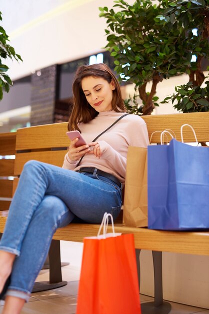 Mujer con teléfono móvil después de grandes compras en el centro comercial