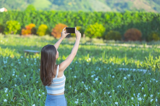 Mujer con teléfono móvil para tomar fotos en el jardín de flores.