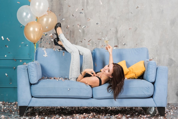 Mujer tendida en el sofá azul con champán
