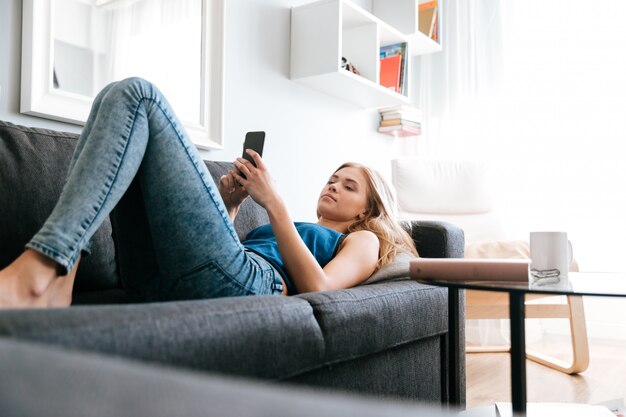 Mujer tendida en el sofá y usando el teléfono celular en casa