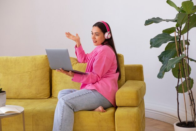 Mujer teniendo una videollamada en una computadora portátil mientras está sentada en el sofá de casa