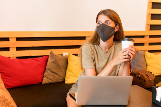 Mujer en terraza con laptop usando máscara