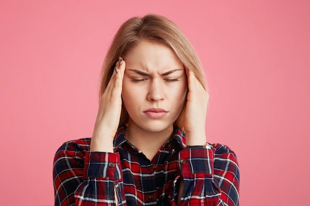 Foto gratuita la mujer tiene dolor de cabeza, mantiene las manos en las sienes, cierra los ojos al sentir un dolor terrible, trabajar demasiado y fatiga