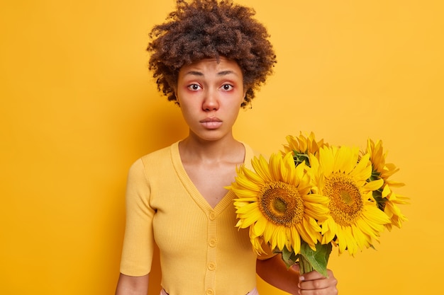 La mujer tiene enrojecimiento alrededor de los ojos, siendo alérgica a los girasoles, usa poses de jumper casual en amarillo vivo