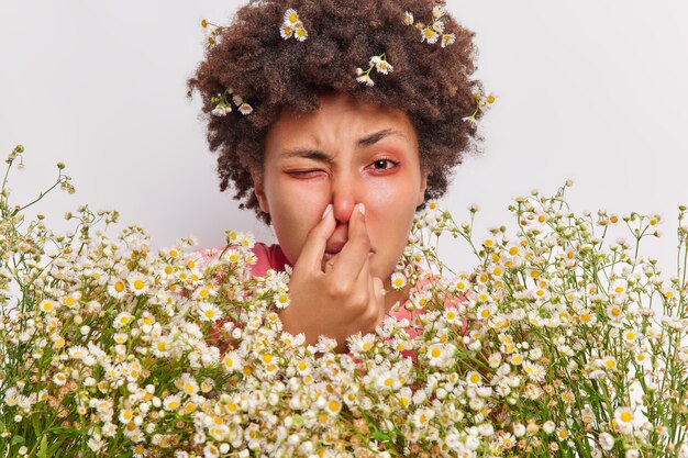 La mujer tiene problemas para respirar. Tiene la nariz. Sufre de alergia a la manzanilla. Tiene un gran ramo de flores. Tiene los ojos enrojecidos.