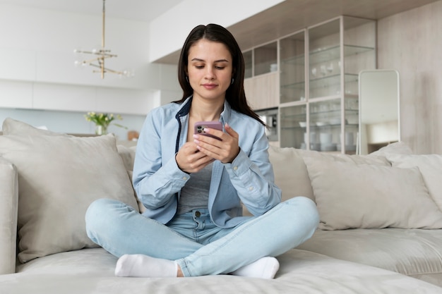 Mujer de tiro completo acostada en el sofá con teléfono inteligente