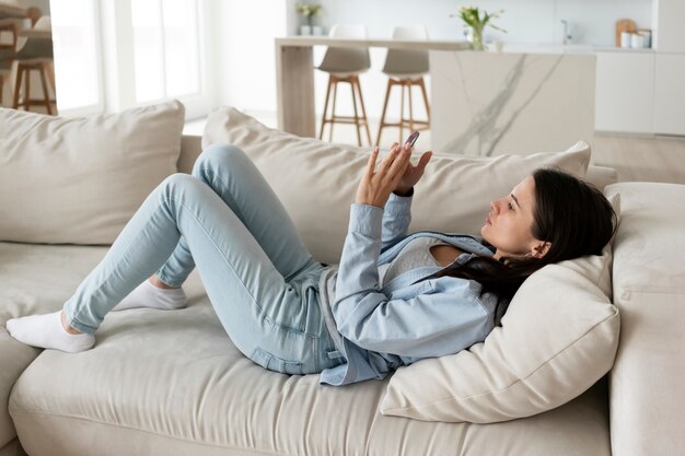 Mujer de tiro completo acostada con teléfono inteligente