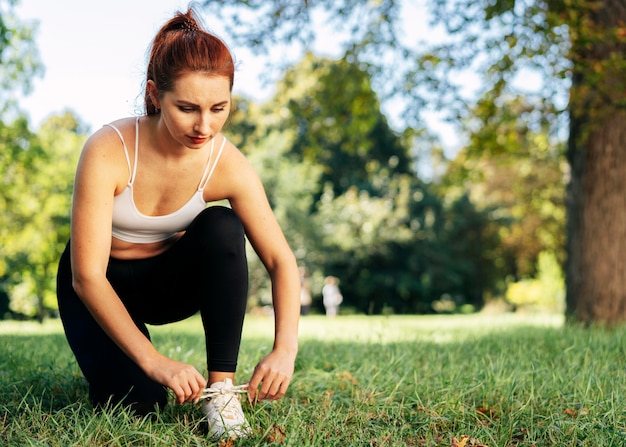 Mujer de tiro completo atando sus cordones fuera