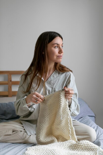 Mujer de tiro completo en la cama tejiendo