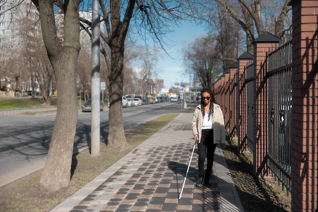 Mujer de tiro completo caminando con bastón blanco.