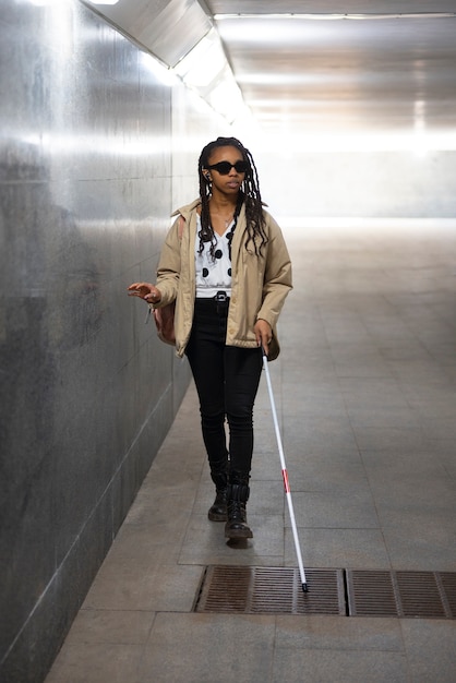 Mujer de tiro completo caminando con bastón blanco.