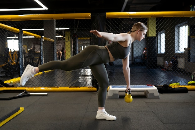 Mujer de tiro completo entrenando con pesas rusas en el gimnasio