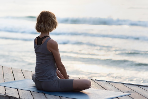 Mujer de tiro completo en estera de yoga frente al mar