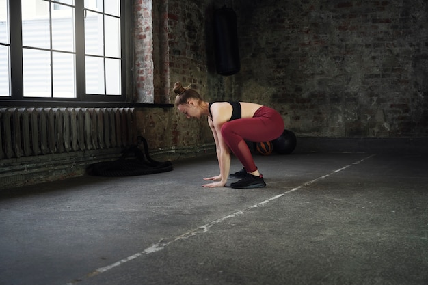 Mujer de tiro completo haciendo burpees en el interior