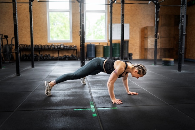 Mujer de tiro completo haciendo burpees en el interior