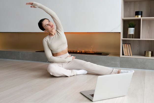 Mujer de tiro completo haciendo ejercicio en casa con computadora portátil