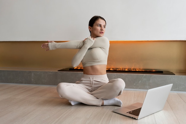 Mujer de tiro completo haciendo ejercicio con computadora portátil en el interior