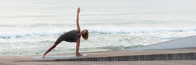 Mujer de tiro completo haciendo pose de triángulo en la playa
