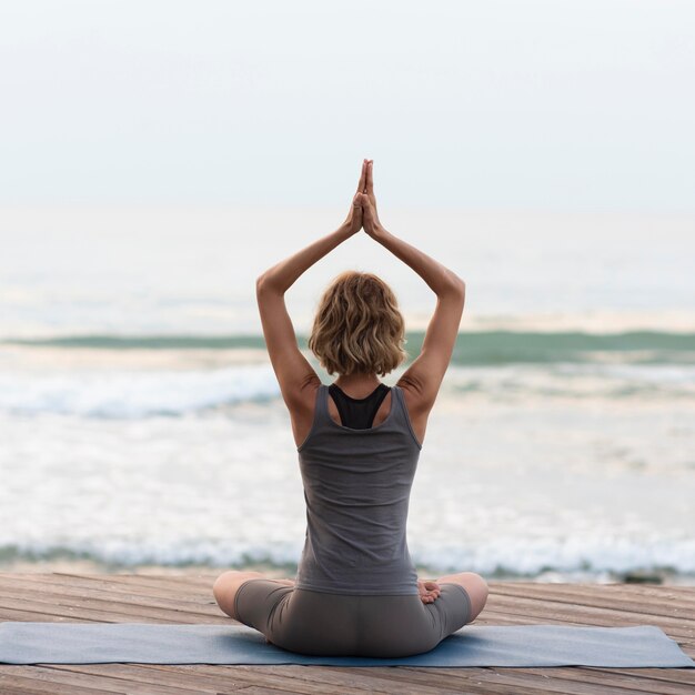 Mujer de tiro completo haciendo sukhasana plantean fuera frente al mar