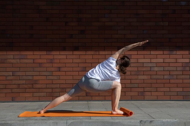 Mujer de tiro completo haciendo yoga al aire libre en la estera