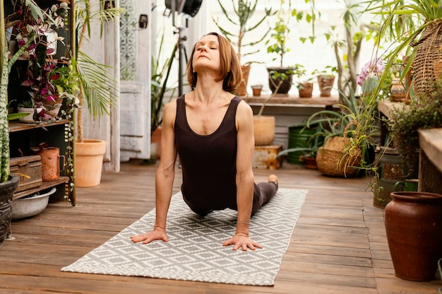 Mujer de tiro completo haciendo yoga en la estera