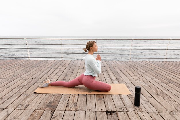 Mujer de tiro completo haciendo yoga en la playa