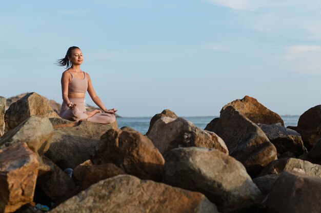 Mujer de tiro completo haciendo yoga en rocas en la naturaleza