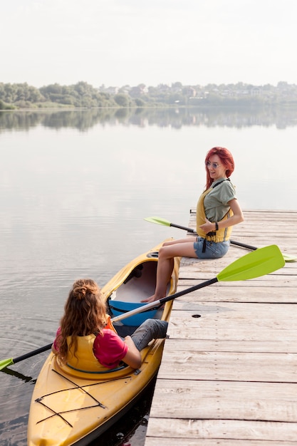 Mujer de tiro completo en kayak con un amigo en el muelle