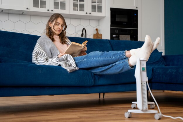 Mujer de tiro completo leyendo cerca del calentador en casa