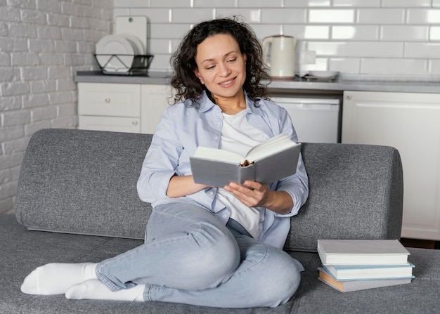 Mujer de tiro completo leyendo en el sofá