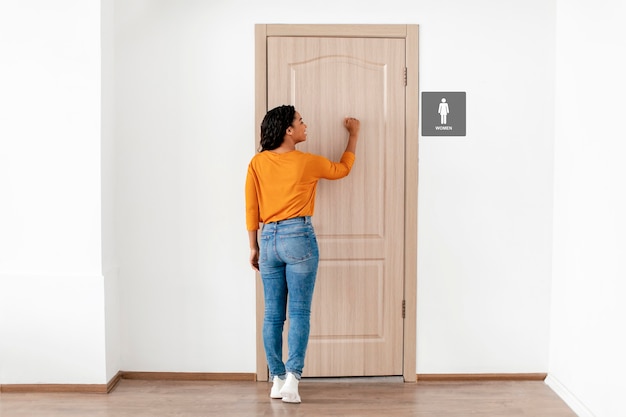 Mujer de tiro completo llamando a la puerta del baño