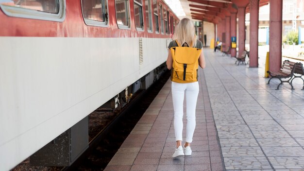 Mujer de tiro completo con mochila caminando por tren