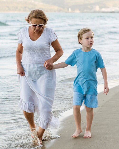 Mujer de tiro completo y niño caminando en la playa