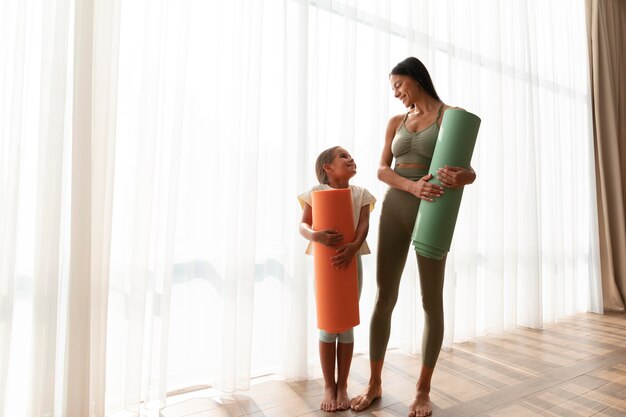 Mujer de tiro completo y niño con estera de yoga