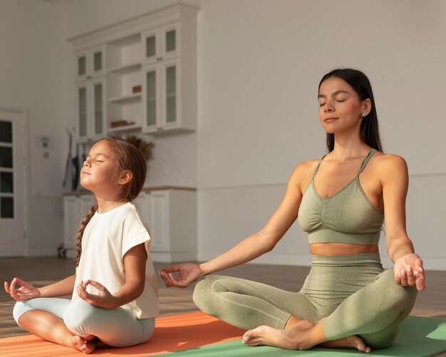 Foto gratuita mujer de tiro completo y niño meditando en casa