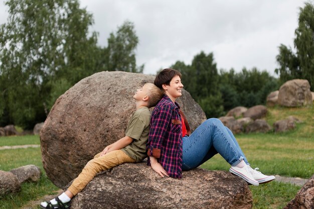 Mujer de tiro completo y niño sentado sobre una roca