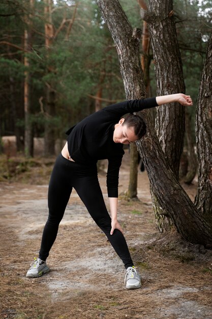 Mujer de tiro completo que se extiende en la naturaleza