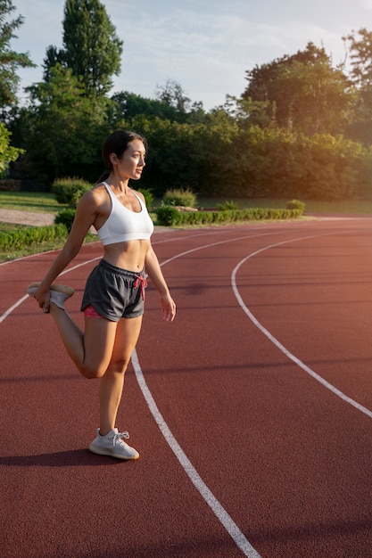 Mujer de tiro completo que se extiende en la pista de atletismo