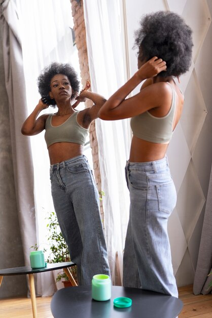 Mujer de tiro completo que peina el cabello afro en el espejo