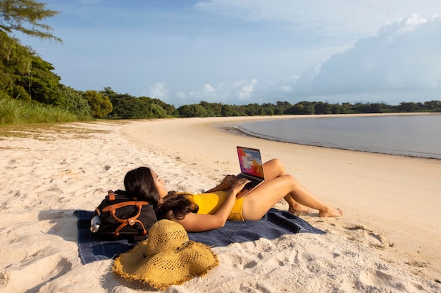 Mujer de tiro completo que trabaja en la playa con un portátil